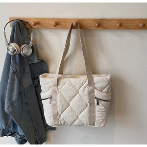 Detailed view of quilted cream tote bag with side zippers hanging on a wooden hook