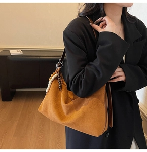 Détail du sac hobo en daim caramel avec breloque en perles de bois porté par un mannequin