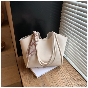 Dettaglio della borsa tote in pelle martellata beige con foulard di seta su un libro