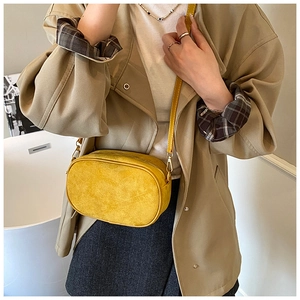 Detail view of yellow frosted suede crossbody bag worn with a beige trench coat