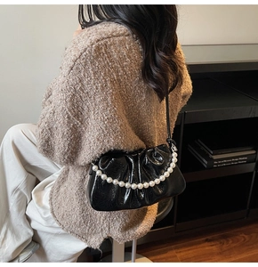 Detail of black glossy pleated crossbody bag featuring elegant large pearl chain strap