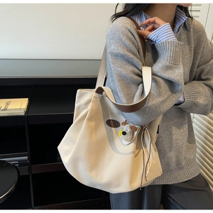 Close-up of beige canvas tote bag with leather logo detail and cute dog plush charm