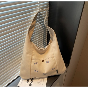 Detail der cremefarbenen Segeltuchtasche mit Vordertasche, braunem Knopf und TELN-Stickerei