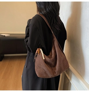 Detail of a dark brown suede hobo bag with ethnic wooden bead pendant on the side