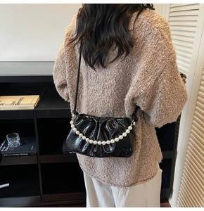 Detail of black pleated shoulder bag featuring elegant pearl chain and glossy finish