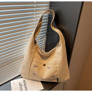 Detailansicht der beigen Canvas-Einkaufstasche mit Vordertasche, Knopf und Stickerei