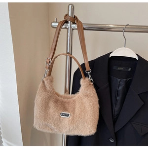 Gros plan sur la texture pelucheuse et le logo en métal d'un sac à main beige en fourrure