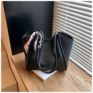 Dettaglio della borsa tote nera in pelle martellata con foulard geometrico su una scala