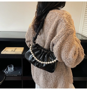Close-up of black pleated patent leather crossbody bag with white pearl chain detail
