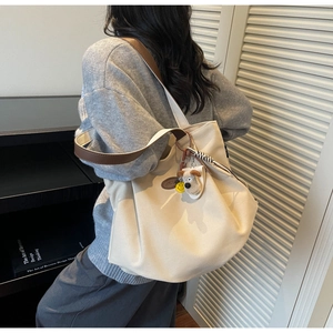Large beige canvas tote bag with brown straps and cute dog charm shown on a model