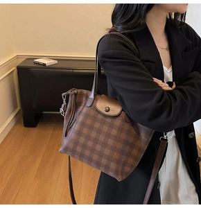 Close-up of brown checkered tote bag featuring leather flap closure and adjustable strap