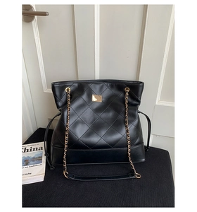 Detail of black quilted tote bag featuring golden chain straps and adjustable side drawstrings