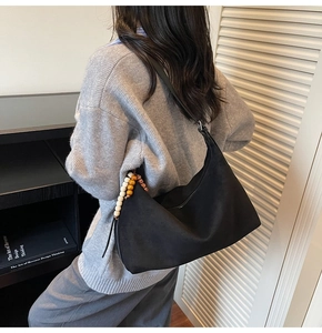 Détail d'un sac hobo minimaliste noir avec des perles en bois vintage sur le côté