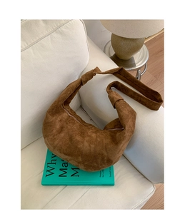 Detail view of the brown suede dumpling bag with quilted texture on a white sofa