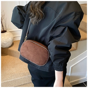 Brown matte suede crossbody bag with gold buckle shown in a lifestyle setting