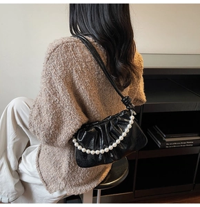Close-up of black pleated cloud bag with elegant pearl chain on woman's shoulder