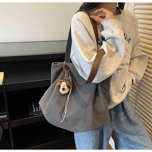 Detail of dark grey canvas tote bag with brown leather strap and puppy plush charm