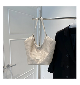 Close-up of cream woven tote bag texture with leather logo patch on a metal hanger