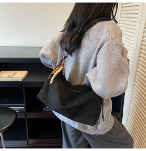 Détail du sac hobo en daim noir avec breloque en perles de bois sur un pull en maille