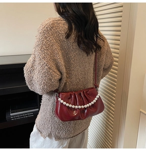 Close-up of a dark red pleated shoulder bag with pearl chain and leather strap