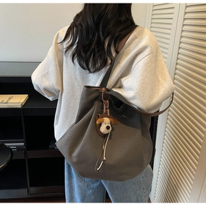 Detail of grey canvas tote bag with brown leather strap and 3D dog plush charm