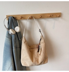 Detail of beige faux suede hobo bag featuring ethnic beaded charm on wooden hanger