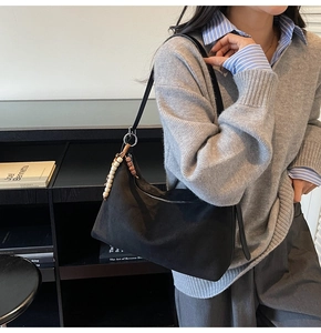 Détail d'un sac dumpling en daim noir avec pendentif perlé porté par un mannequin