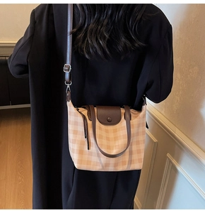 Detail of gingham tote bag with brown leather straps worn over a black winter wool coat