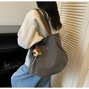 Detail of grey canvas tote bag with brown leather straps and cute dog plush pendant