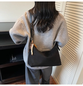 Détail d'un sac hobo en daim noir avec pendentif perlé porté à l'épaule sur mannequin