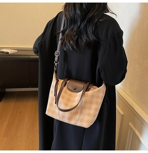 Detail of checkered tote bag with brown leather trim and button closure on model
