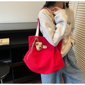 Detail of red canvas tote bag featuring white straps and plush cartoon puppy charm pendant