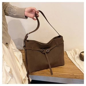 Detail of deep brown frosted leather tote bag with elegant silver buckle on wooden desk