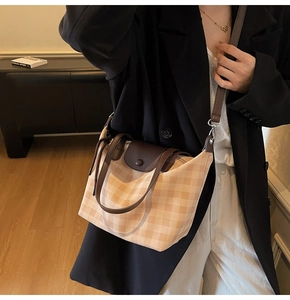 Detail view of plaid tote bag with brown leather flap and adjustable crossbody strap