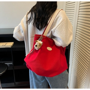 Detail of red canvas tote bag featuring creamy leather straps and a plush puppy charm