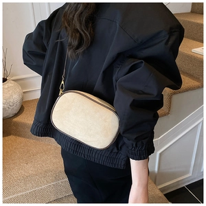 Beige camera bag with dark piping shown on a model wearing an oversized black blazer