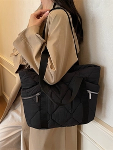 Quilted black tote bag with dual silver zippers and wide shoulder strap shown on model