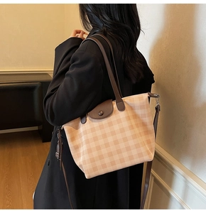 Checkered tote bag with adjustable long strap and brown leather handles in a side view
