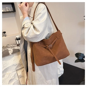 Brown matte leather tote bag with buckle detail worn by a model in a cozy cafe
