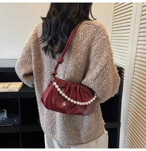 Detail of burgundy pleated shoulder bag with oversized pearl chain and glossy finish