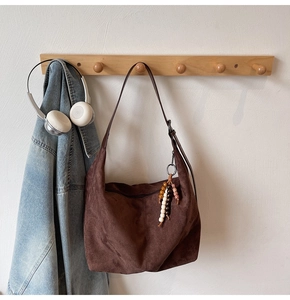 Detailed view of dark brown suede tote bag with ethnic beaded tassel hanging on wall