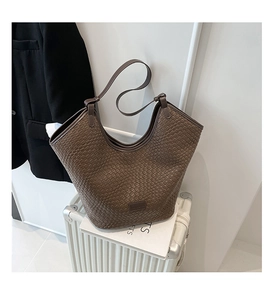 Detailed close-up of dark brown woven tote bag with smooth leather logo patch on luggage