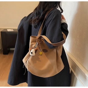 Detailed view of brown canvas tote bag featuring decorative pendants on a shoulder strap