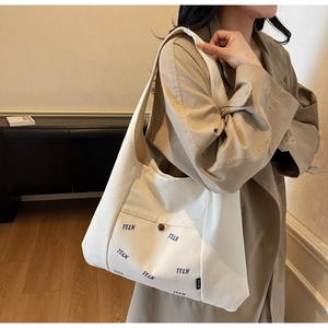 Detailansicht der großen weißen Canvas-Tasche mit Buchstabendruck und Vordertasche