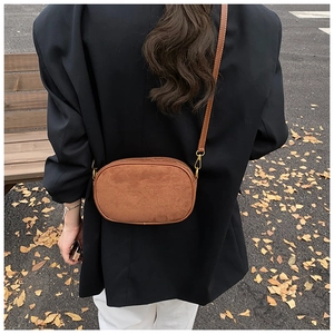 Close-up of brown suede crossbody bag with leather strap against black blazer background