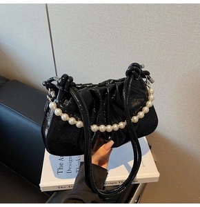 Detail of black patent leather pleated bag with large pearl strap and slim shoulder straps