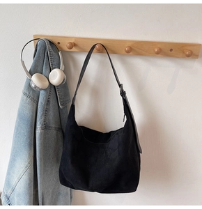 Detail of black faux suede Hobo shoulder bag hanging on a wooden hook in a cozy room