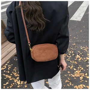 Close-up of brown suede oval crossbody bag with adjustable strap on a black blazer
