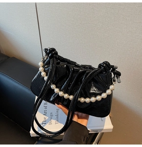 Detail of black glossy pleated handbag with elegant large pearl chain decoration