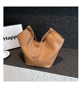 Detail of a brown woven leather tote bag showing intricate textures on a rocky surface
